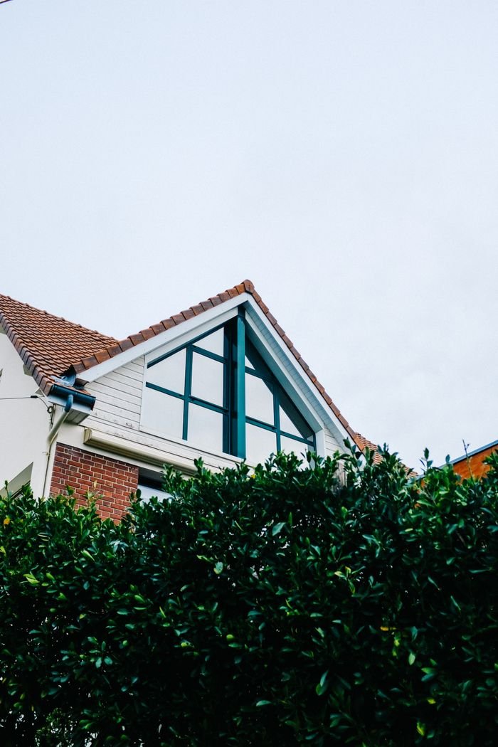 service-03 A picturesque view of a brick house with a gabled roof surrounded by lush greenery.
