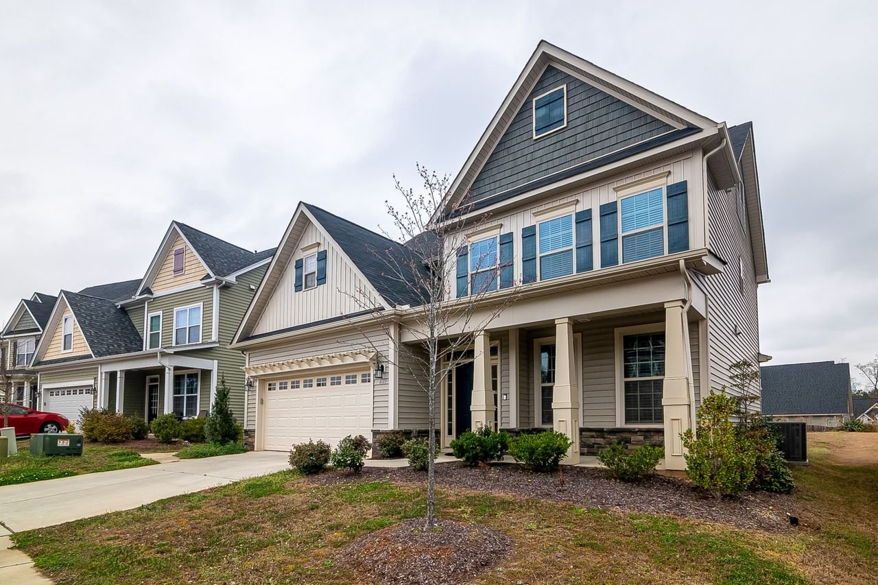 A row of modern suburban homes with garages, driveways, and landscaped lawns in daylight.